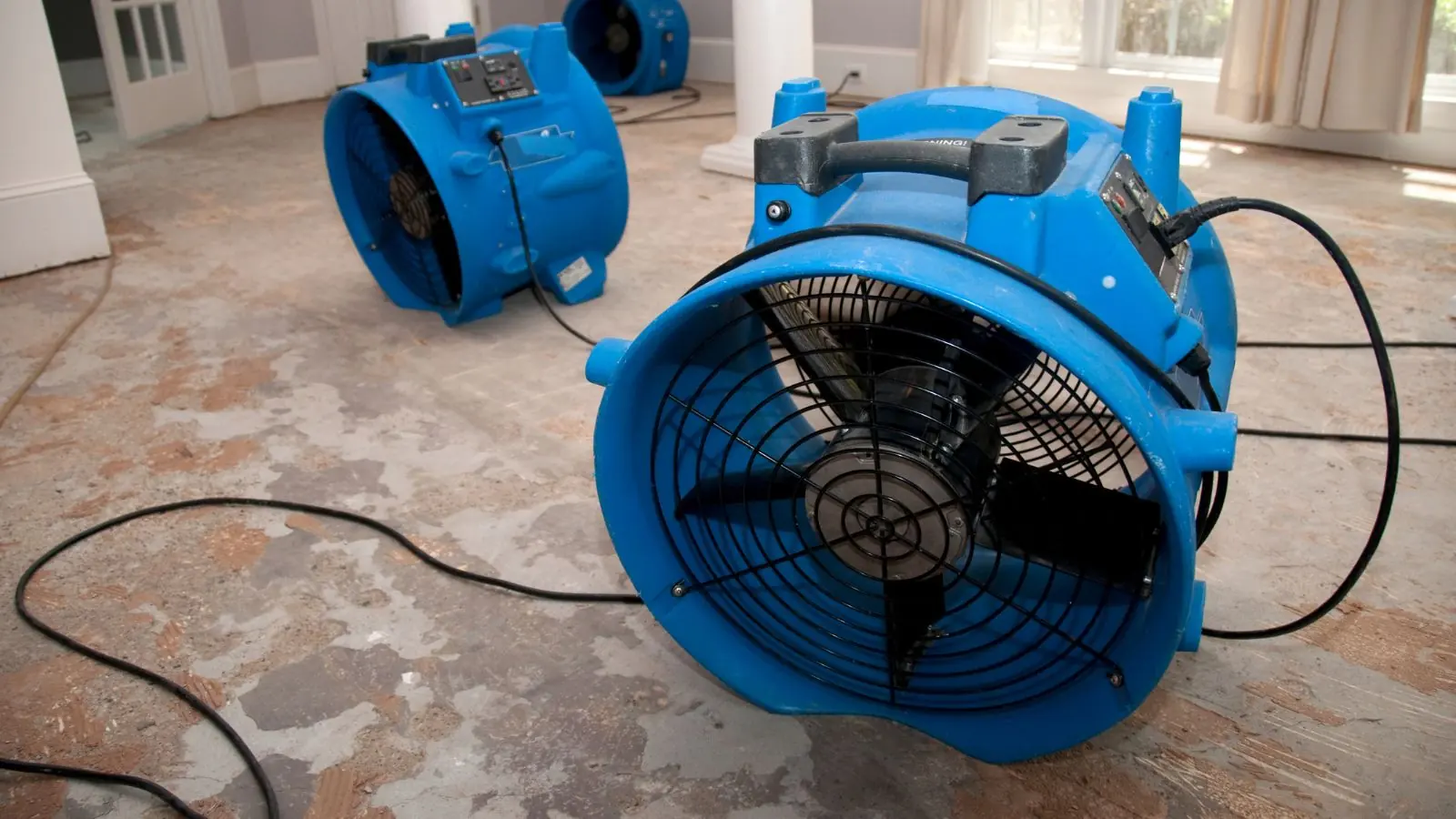 Blue air mover running on a bare floor to dry out a room